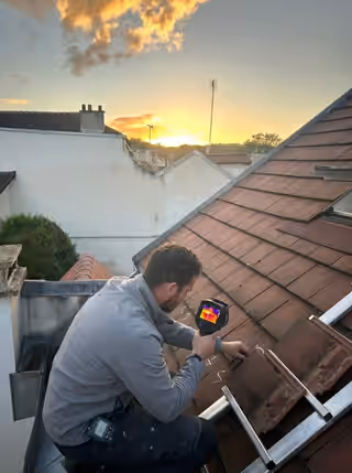 Couvreur sur un toit en tuiles, une caméra thermique à la main pour localiser une infiltration