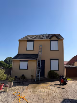 Maison à étage avec une échelle contre la façade et un nettoyeur au pied, toiture nettoyée